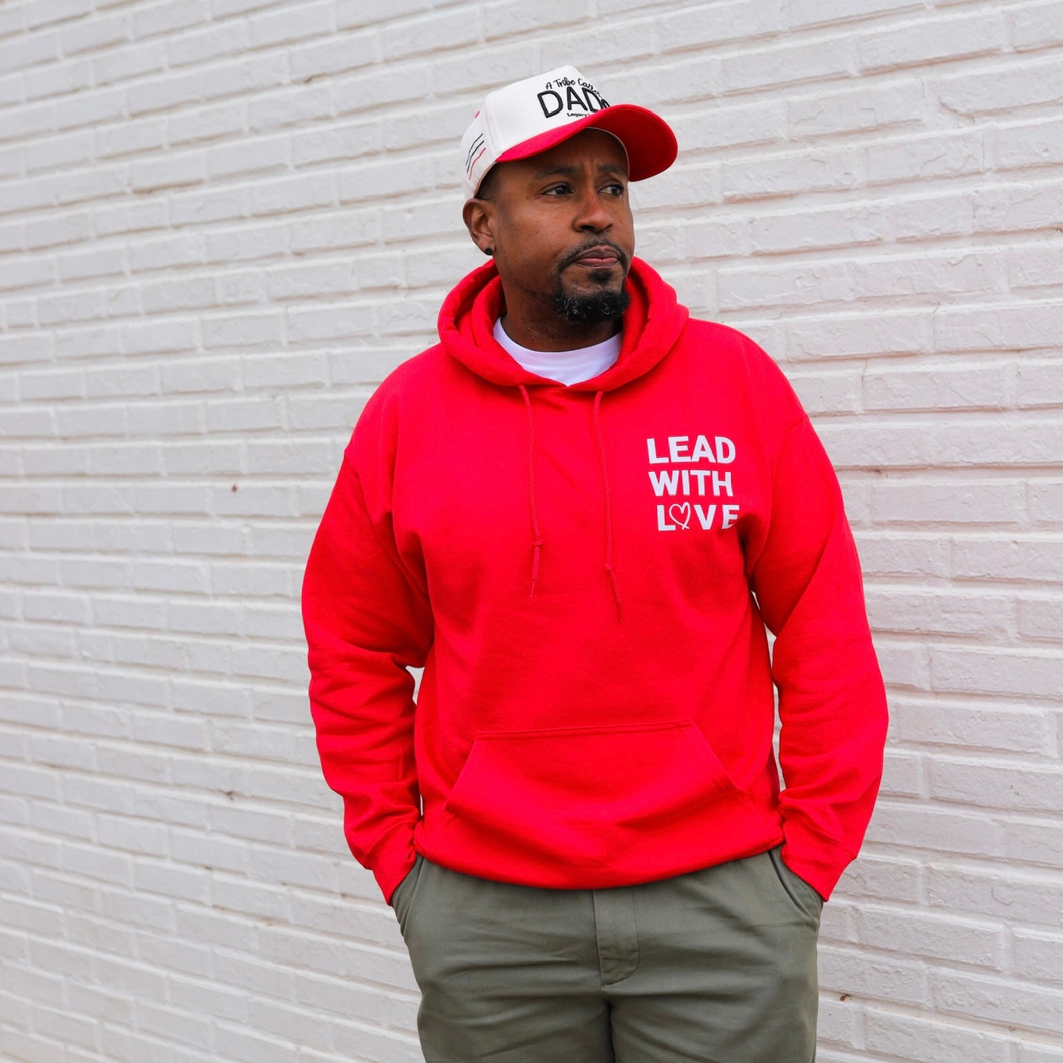 Man wearing a red hoodie with 'Lead with Love' text against a light brick wall.