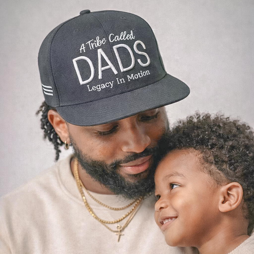 Man wearing a cap with 'A Tribe Called DADS' text, looking at a child against a neutral background
