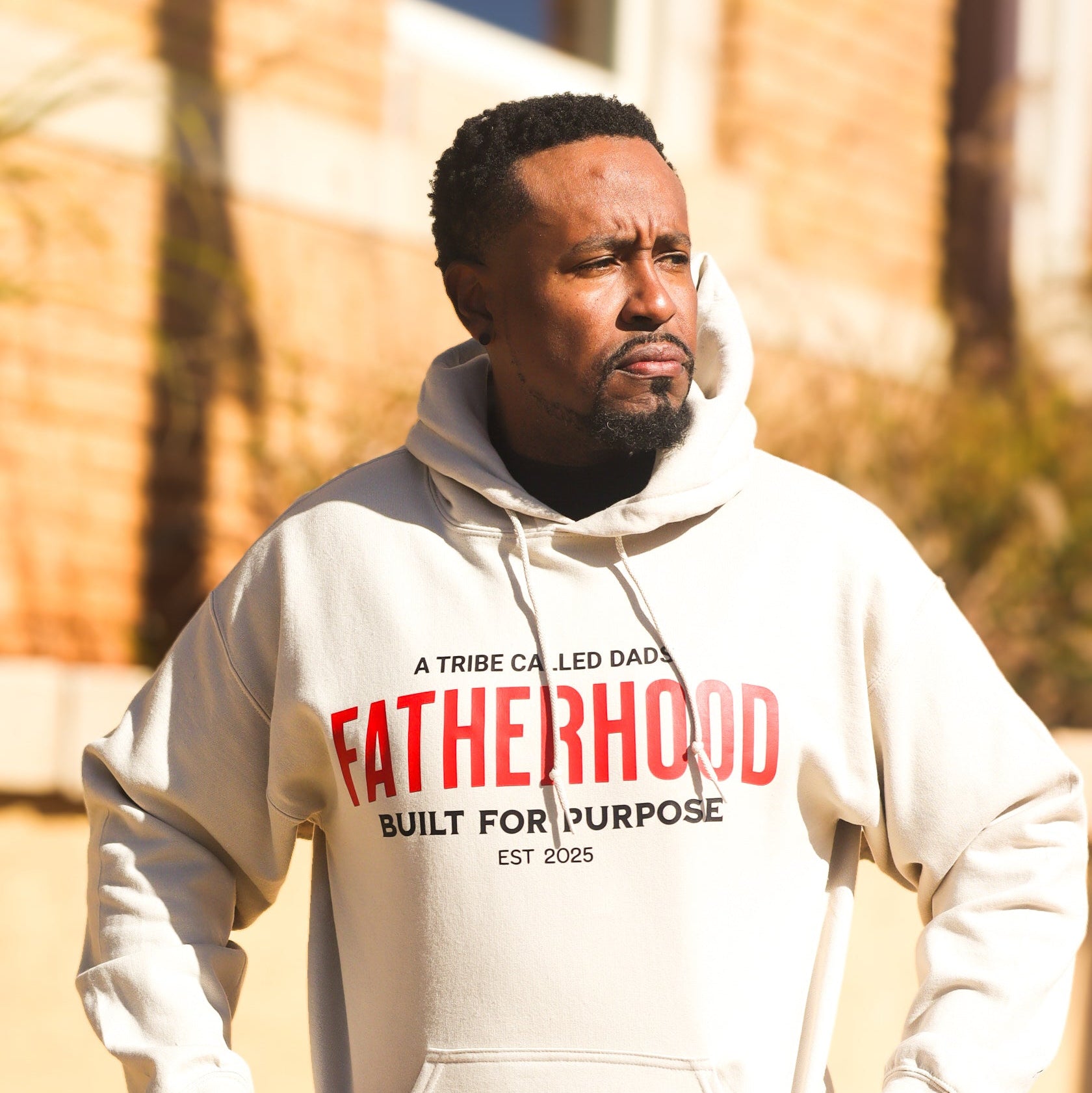 Man wearing a hoodie with 'Fatherhood Built for Purpose' text outdoors.